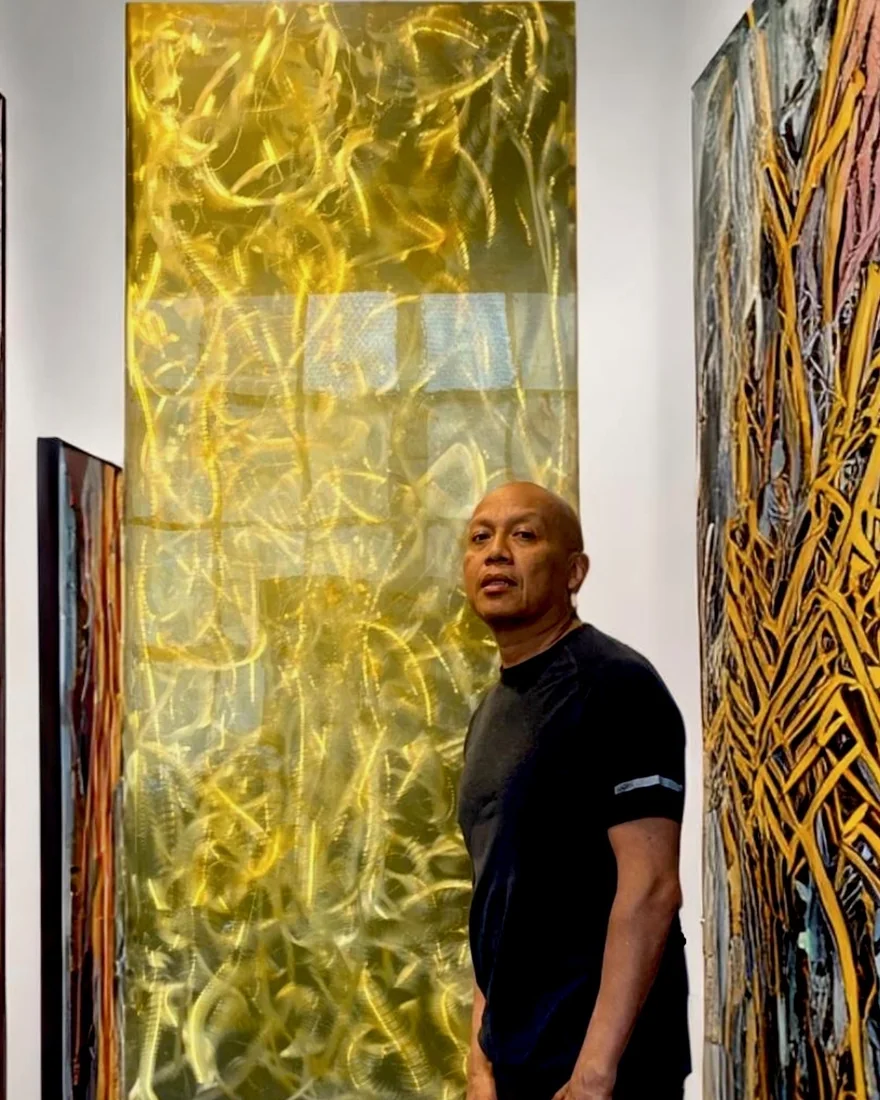 Andre Kowlessar in his studio among several large works, a red painting on the easel