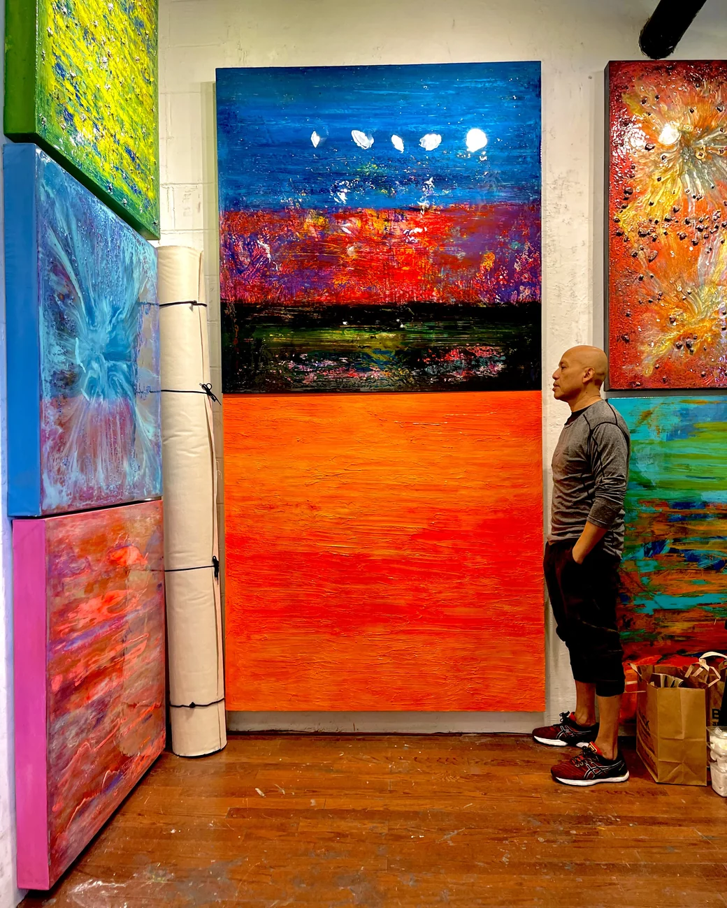 Andre Kowlessar standing between two large-scale works in his studio